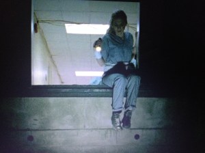 We see poor Beth, dressed in prison-looking scrubs, peering down a steep elevator shaft, looking for a way out of what looks like Hell.