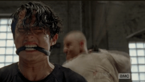 The butchers line up behind Glenn, who clenches his teeth, anticipating the blow.