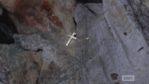 Gabriel manages to throw the walker off him, and picks up a large rock, ready to smash her head in, then spots the gold cross around the walker's neck...she may have been one of his parishioners that he locked out of the church...