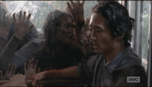 Glenn tries to think of a way as the walkers paw and push, trying to get at them.