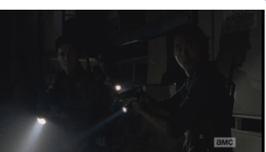 Glenn hears the faint sound of walkers, somewhere in the building. He motions to the rest to be quiet, listens.