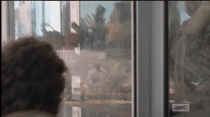 Glenn rams the butt end of his rifle into the glass of the revolving door again and again, but is unable to break the glass.