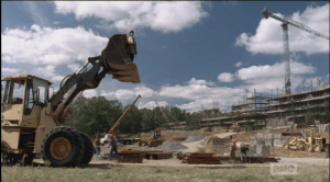 ...the men load the materials, to bolster a compromised section of the wall, while a woman stands watch high in an excavator bucket.