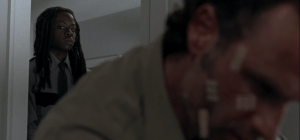 Rick is sitting alone, looking down, thinking. Michonne comes up behind him, watches him a moment.
