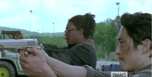 As the walkers crash through the storefront window and lurch towards them, Glenn blows a walker's brains away...perfect aim.