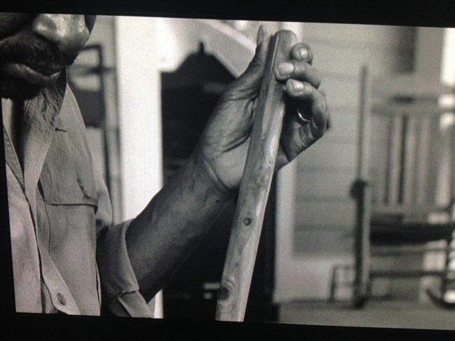 This scene shifts to the past, where Morgan sits outside on Rick's porch, polishing his staff.