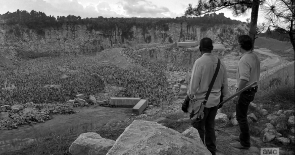 The men approach the edge before a steep drop into a deep quarry, where thousands of walkers are, below, snarling and milling about, trapped in all sides by steep embankments, piles of rock, and serendipotously placed tractor trailers.